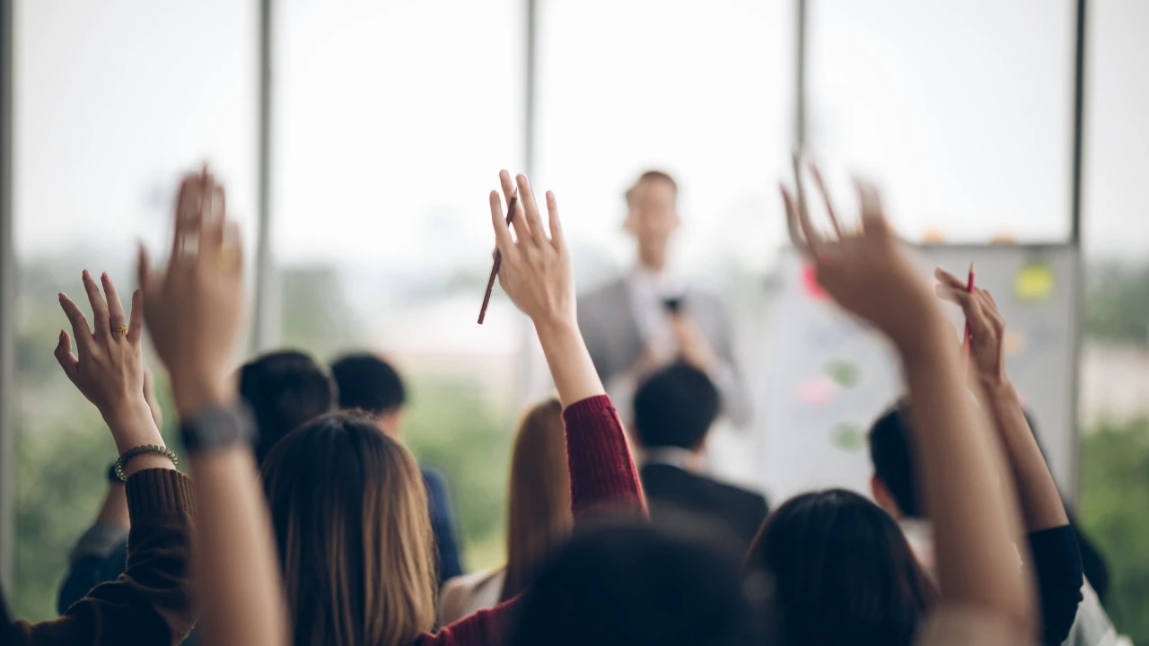 Mitarbeiter heben im Team-Workshop die Hand und stellen Fragen